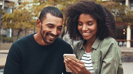 A man and a woman laughing and looking at a smartphone