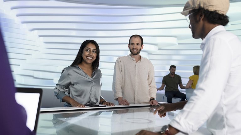 A man and a woman stand in a room at a table with a touch screen
