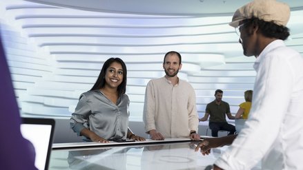 A man and a woman stand in a room at a table with a touch screen