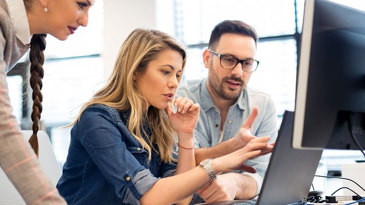 Employees gather around a computer screen and discuss 