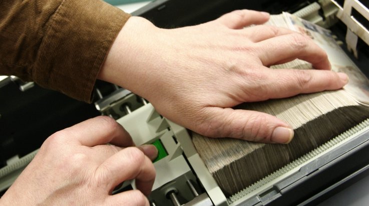 A man operates a banknote processing system with Brazilian reais