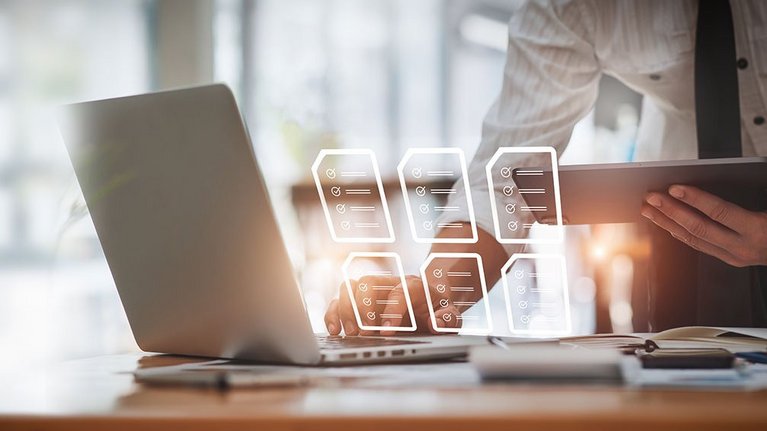 A man holds a tablet in one hand and operates a laptop with the other