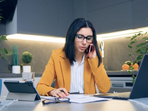 A businesswoman operates her laptop and makes calls on her smartphone in her office at home