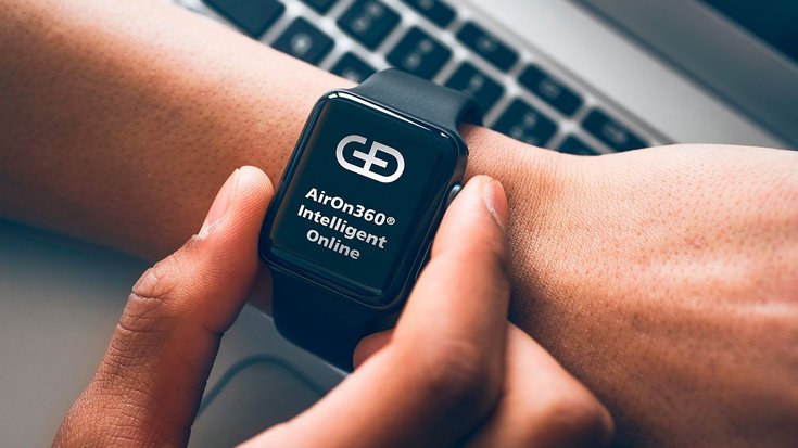 A person adjusts a smartwatch displaying the logo and text "Airon360® Intelligent Online" on its screen.