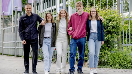 Five young people walking arm in arm on the sidewalk
