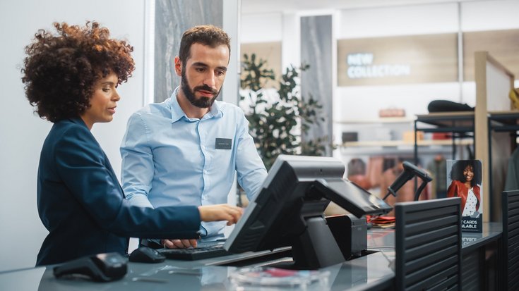 Two employees working together at a retail checkout counter