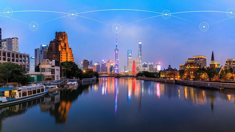 Panoramic view of a city skyline at dusk with illuminated buildings and a river in the foreground, connected by digital network symbols.