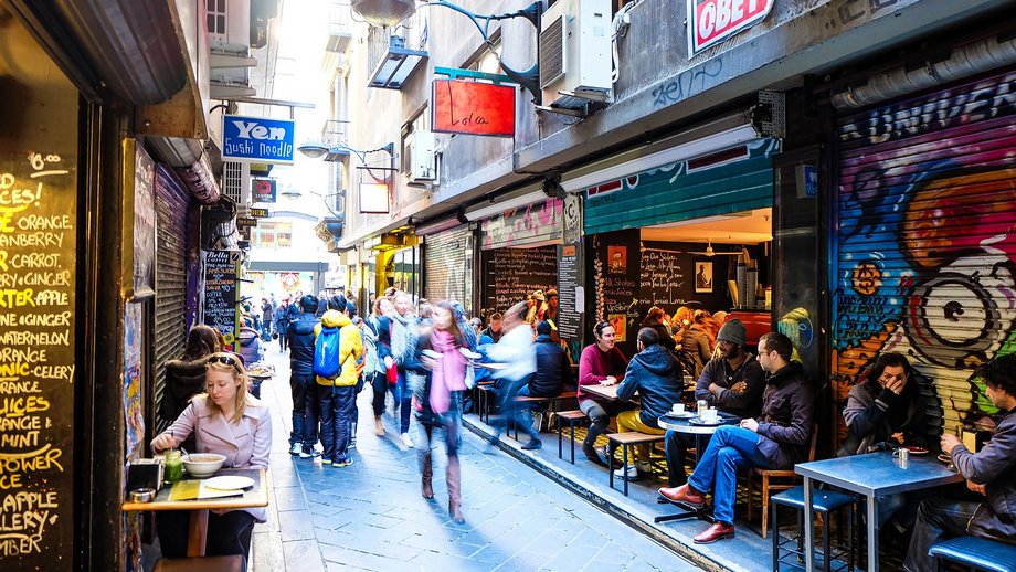 A bustling laneway with outdoor diners and colorful shopfronts.