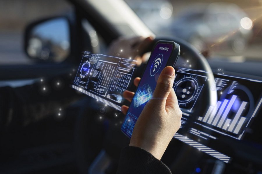 Hand holding smartphone in car with digital displays.