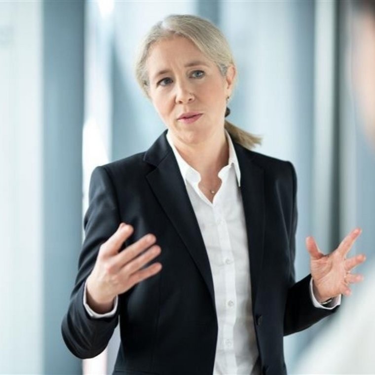 Gabrielle Bugat in business attire, gesturing while speaking in a modern office setting
