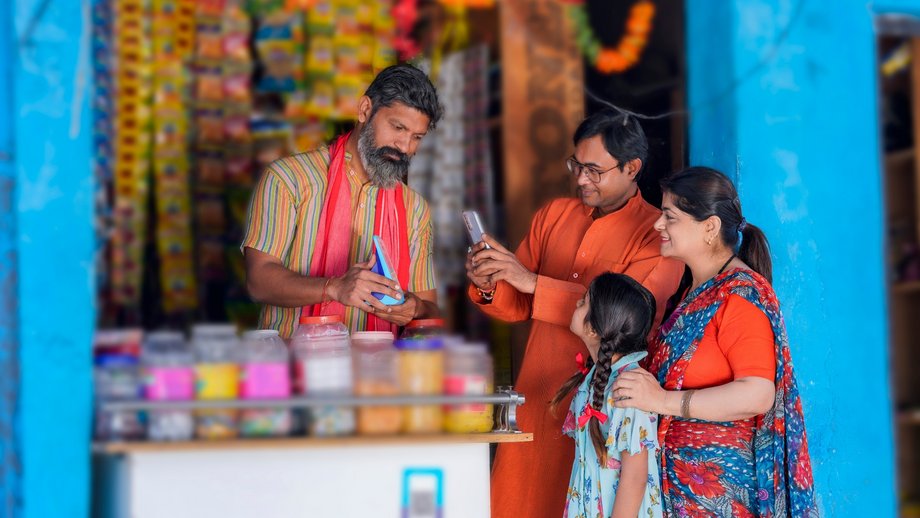An Indian shopkeeper shows a customer and his family how they can pay easily with their smartphone.