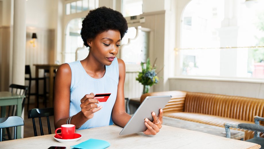 Woman drinking coffee and using a tablet in a café to pay for her order.