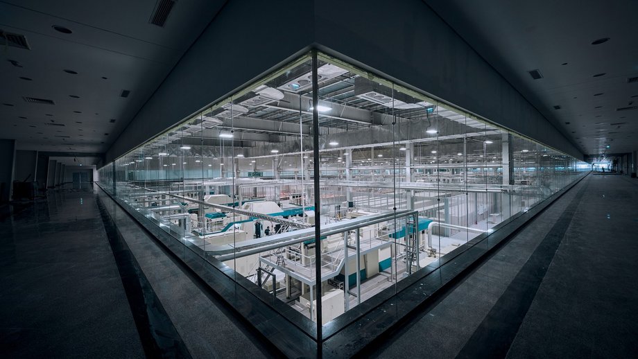 A modern cash center with state-of-the-art equipment, viewed from a long glass-walled hallway. The facility is well-lit and a few people are visible inside