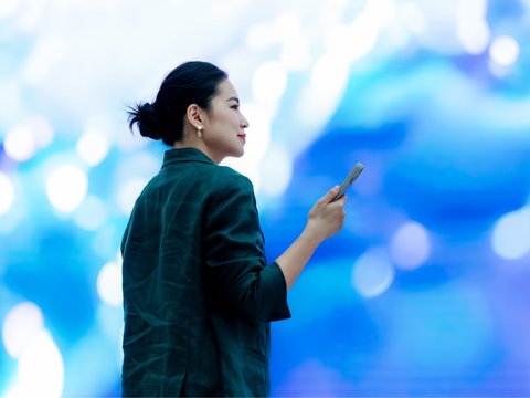 Asian businesswoman with smartphone standing in front of a big screen, doing an instant payment