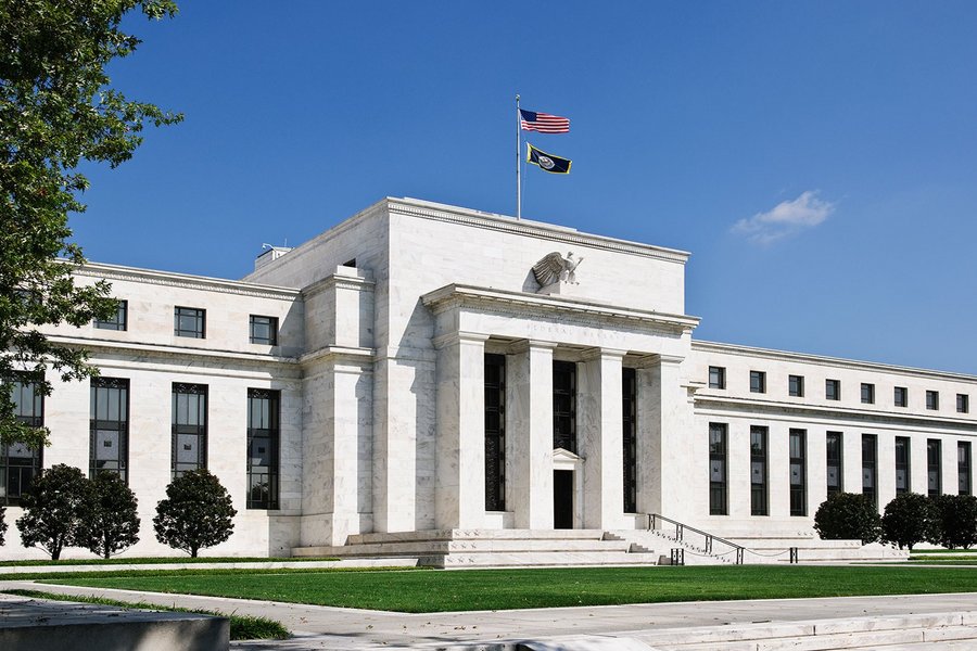 The main entrance of the US Federal Reserve, surrounded by trees, with an American flag hoisted
