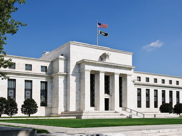 The main entrance of the US Federal Reserve, surrounded by trees, with an American flag hoisted