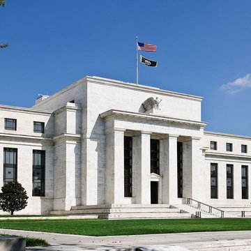 The main entrance of the US Federal Reserve, surrounded by trees, with an American flag hoisted