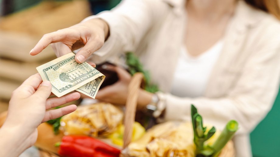 A woman with a shopping basket pays the cashier at the checkout with cash