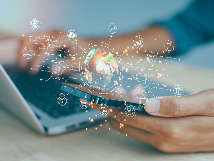 Person using a laptop and smartphone with a digital globe and network icons in the foreground.