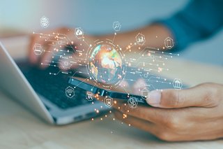 Person using a laptop and smartphone with a digital globe and network icons in the foreground.