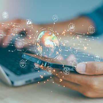Person using a laptop and smartphone with a digital globe and network icons in the foreground.
