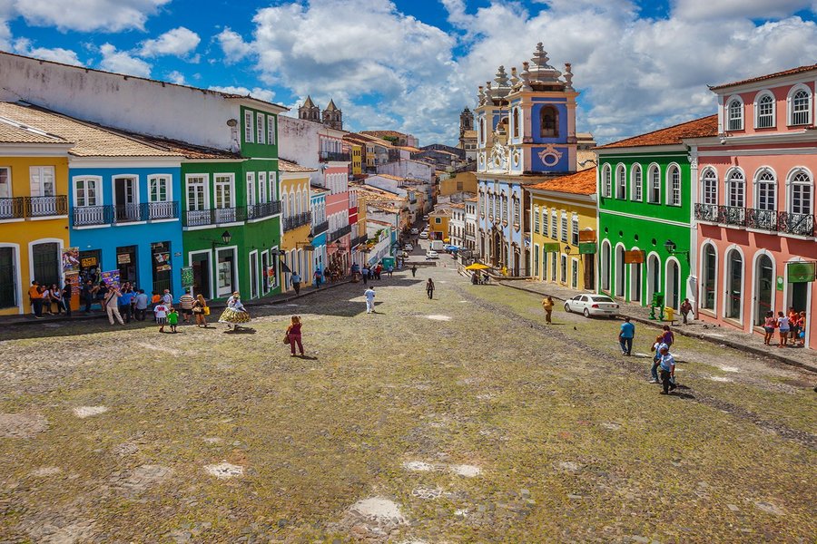 A vibrant street scene in Pelourinho, Salvador, Brazil, with colorful colonial buildings and people walking under a bright blue sky.