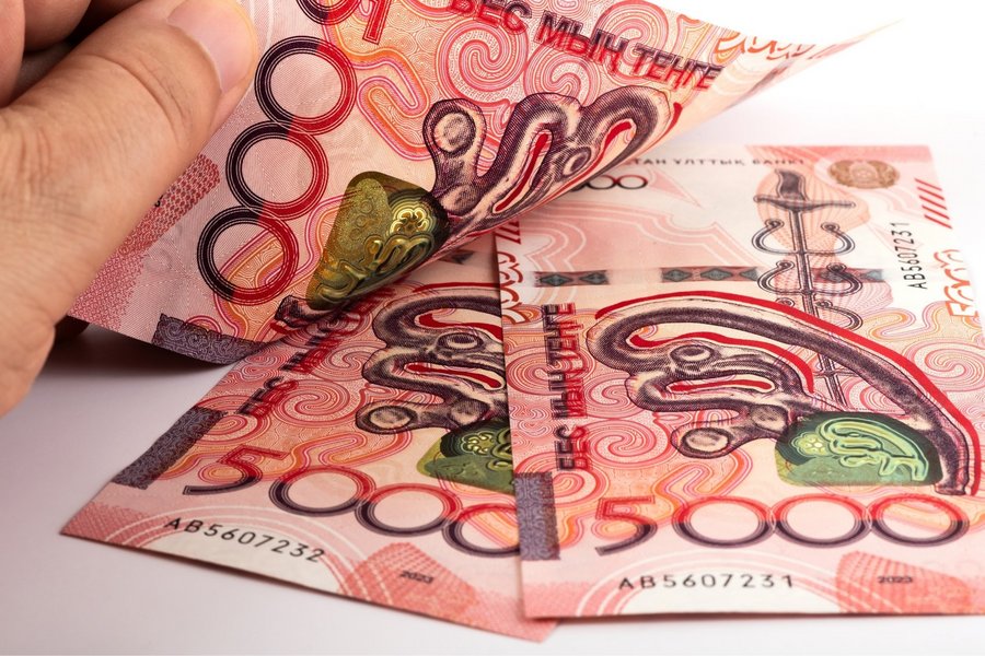 Three red new Kazakh 5000 Tenge banknotes with a man’s hand on them.
