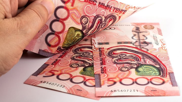 Three red new Kazakh 5000 Tenge banknotes with a man’s hand on them.