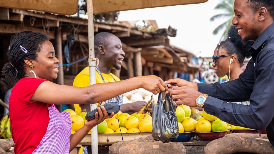 Female market vendor accepting a digital payment from a customer while buying fruits.
