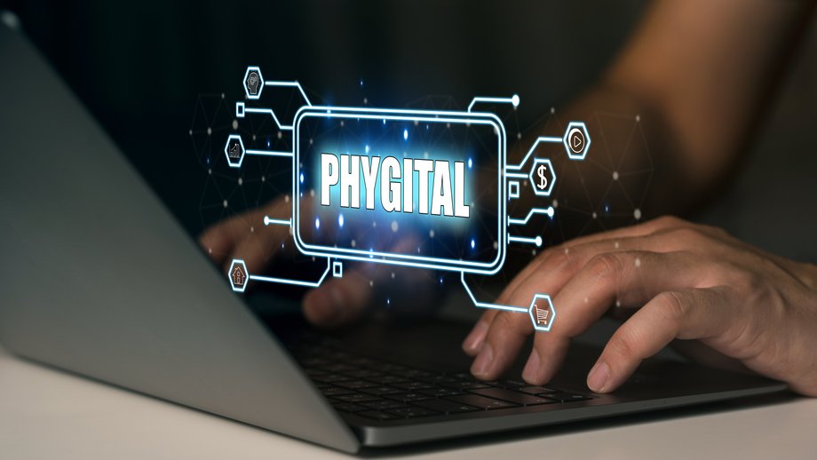 Laptop, with “Phygital” in a glowing digital font, surrounded by symbols
