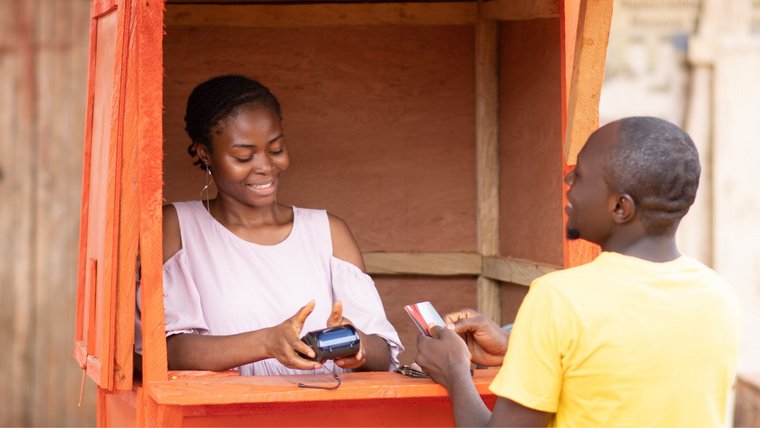 A man hands his credit card to a woman at a POS service kiosk for cash withdrawal