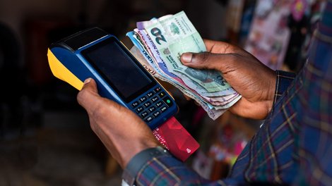 A man holds a point-of-sale (POS) terminal and Nigerian naira banknotes in his hands
