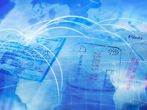 A passport full of different stamps lies on a blue colored world map with travel destinations.