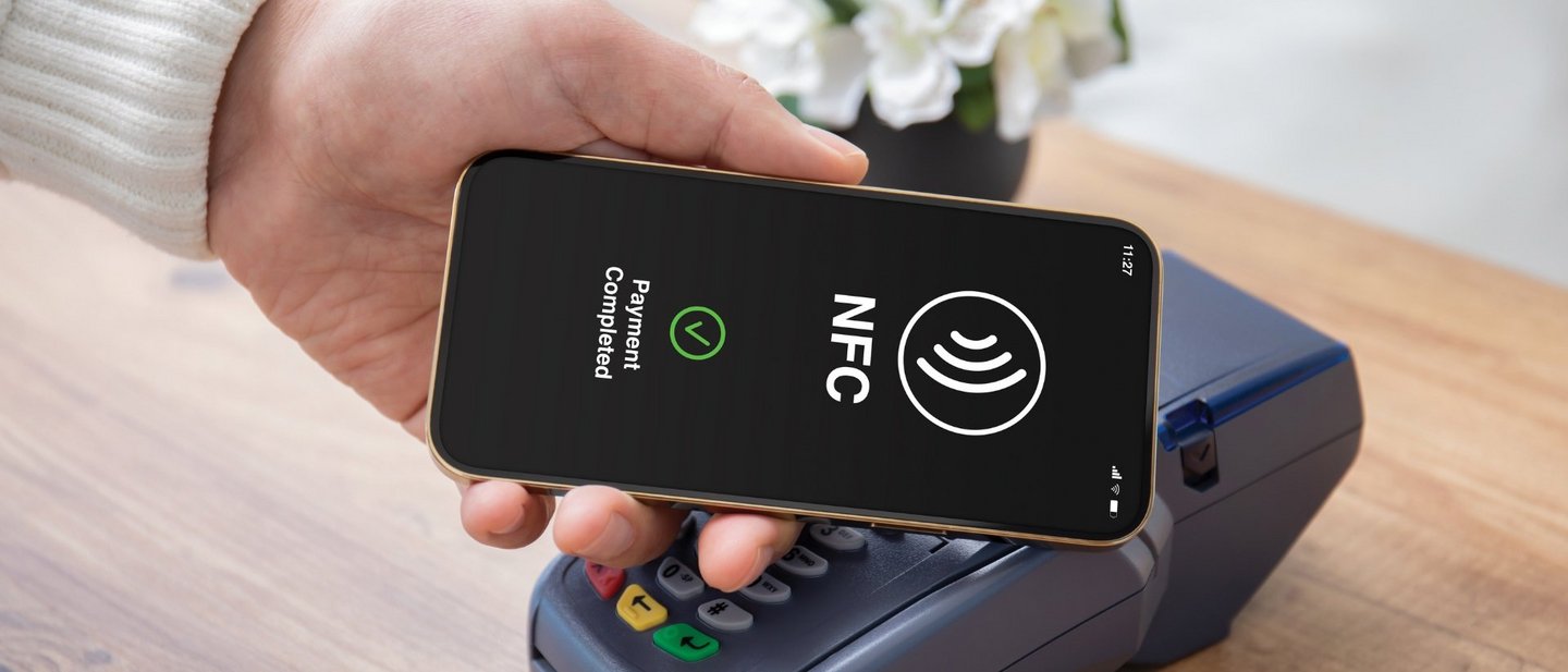 Male hand holds a smartphone to a pos terminal in order to pay via wireless technology (NFC)
