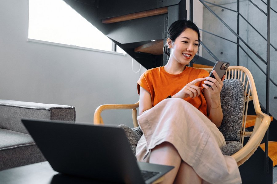 Person sitting in chair using smartphone next to laptop