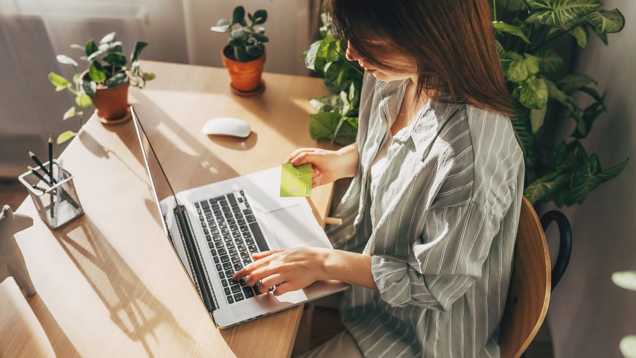 Woman sitting at a laptop and using a green payment card