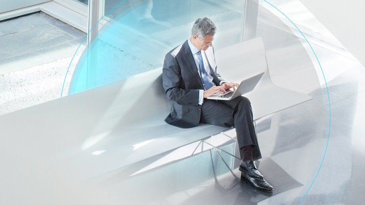 man in suit sits on a bank and types into his laptop