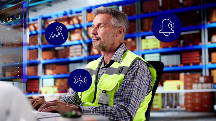 Picture of a warehouse worker in a high-visibility vest checking a tracking dashboard on a digital screen