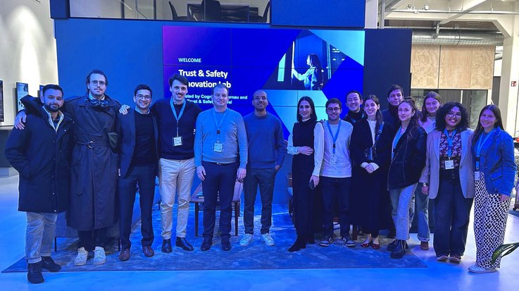 Large group of people standing in front of a digital screen displaying 'Trust & Safety Innovation Lab' at a corporate event.