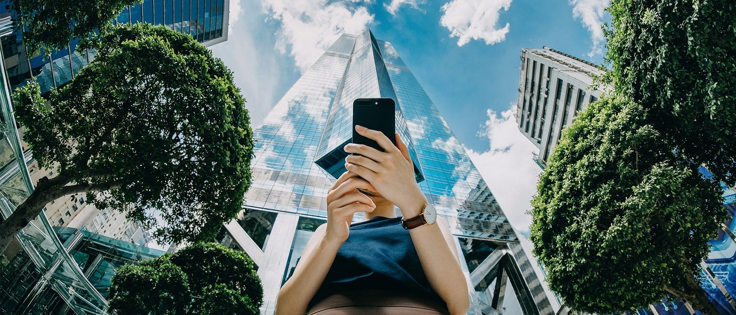 Confident young businesswoman using mobile phone in front of highrise financial towers in Central Business District on a fresh bright morning