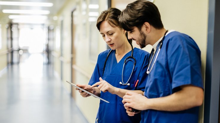 Two medical staff look at a tablet in a medical setting.