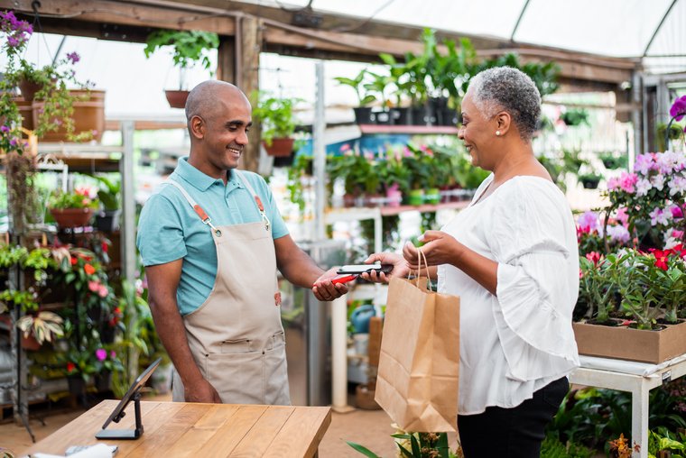 A woman is paying for goods with her smartphone at a flower store.