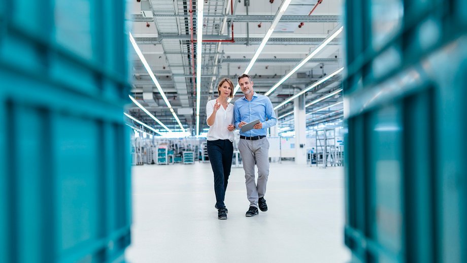 Businessman and businesswoman with tablet talking in a factory hall
