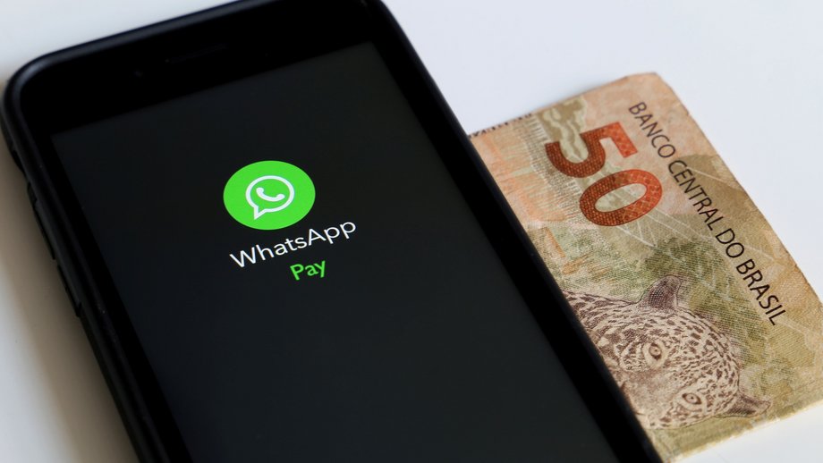 Smartphone displaying WhatsApp Pay with a 50 Brazilian Real banknote beside it