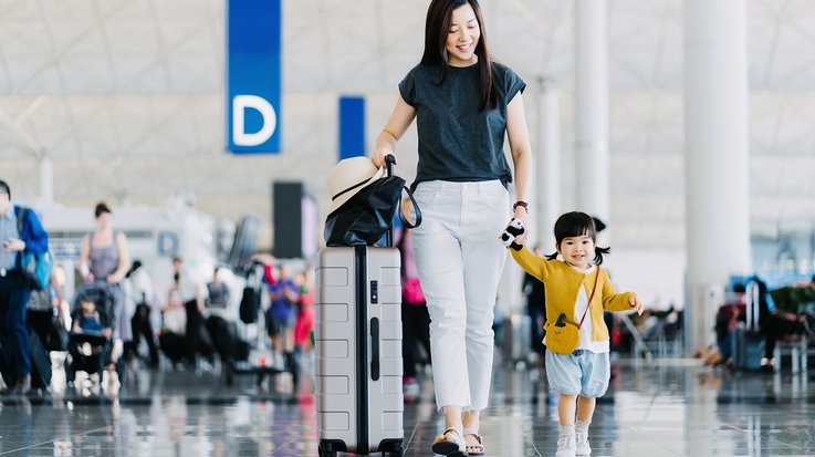 Joyful mother holding hands of her daughter, walking through airport concourse and traveling by plane on a vacation.