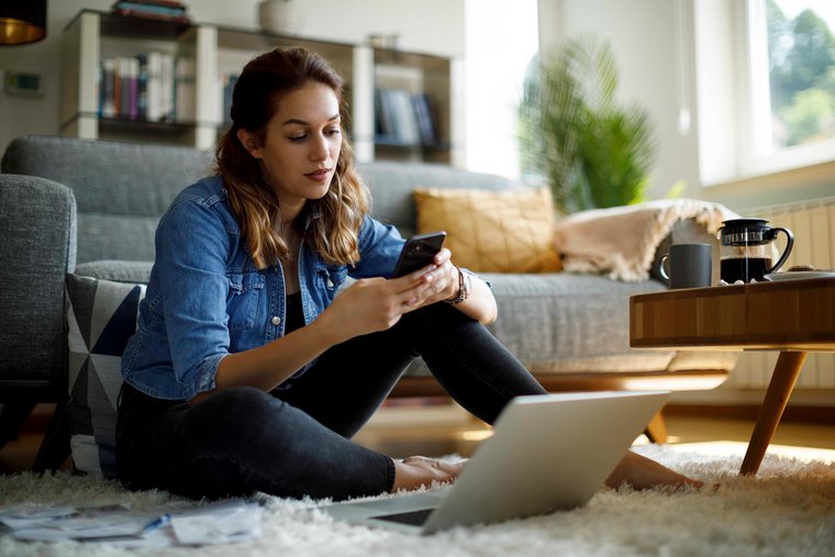 A young woman sitting on the floor with a mobile in her hands.