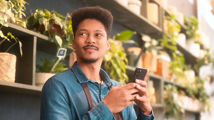 A young man holding a smartphone in a plant shop