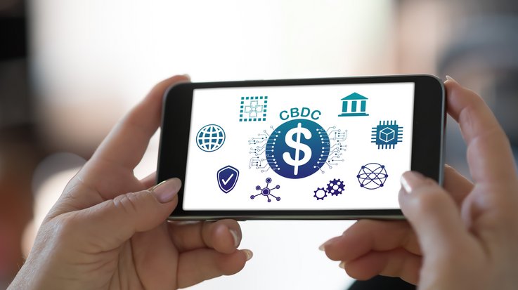 Someone is holding a smartphone with 'CBDC' written on the screen, surrounded by various symbols