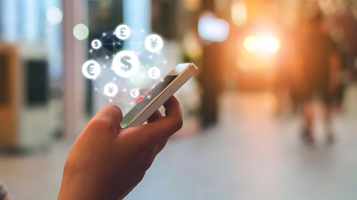 Someone operates a smartphone with symbols for various currencies hovering above it