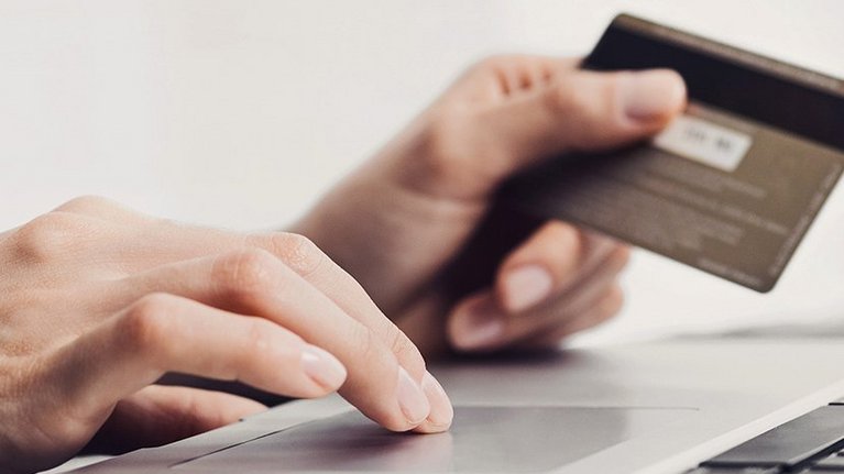 Two hands, one operating the keyboard of a laptop, the other holding a credit card